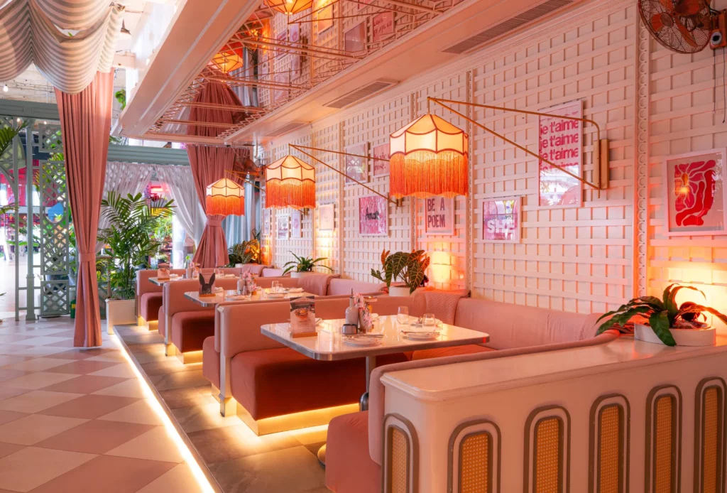 View of Mami Rose DJ booth surrounded by dining tables and speakers under pink lighting.